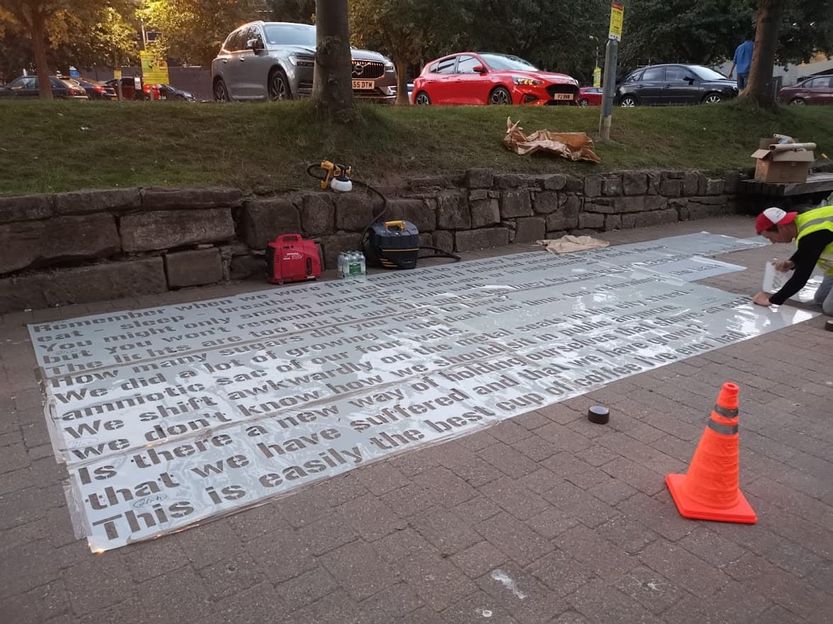 Large poem being stencilled onto pavement with white letters
